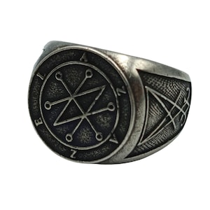A silver ring with a sigil design on the face. The Azazel sigil ring is a star with a triangle inside and the letters. The band of the ring has a more intricate design.