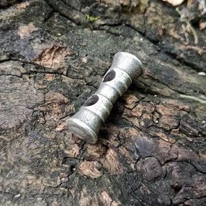 May include: A silver metal bead with two holes, designed for use in jewellery making.