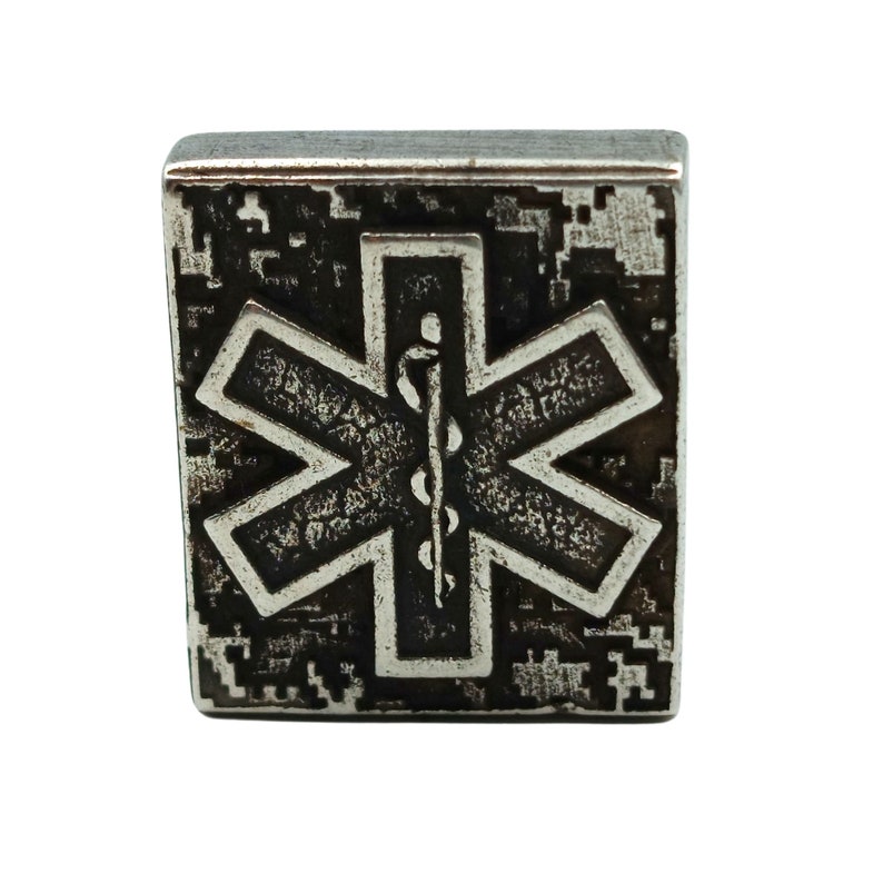 Pode incluir: Um amuleto quadrado de metal prateado com um s&iacute;mbolo m&eacute;dico de estrela da vida preto e branco. O amuleto tem um acabamento texturizado e desgastado.