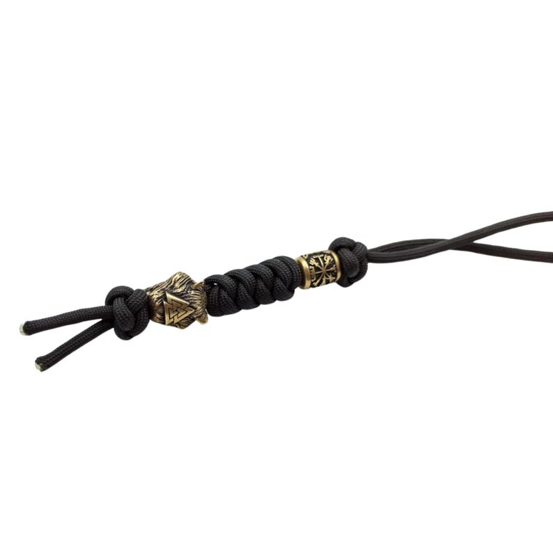 May include: Black paracord keychain with a brass bead featuring a wolf head and a symbol, and another brass bead with a symbol.