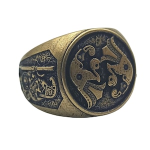 May include: A gold-toned ring with a black and gold design. The ring features a circular design with intricate patterns and a raised edge.