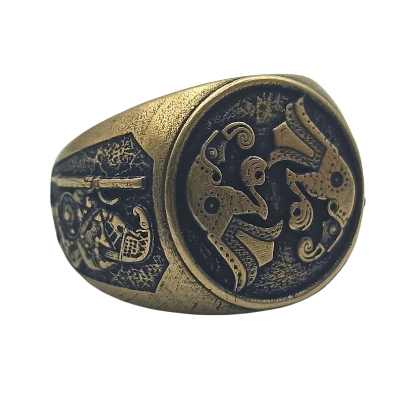 May include: A gold-toned ring with a black and gold design. The ring features a circular design with intricate patterns and a raised edge.