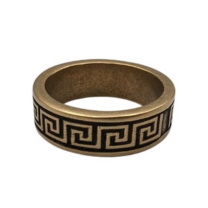 May include: A wide band ring crafted from a metallic material with a muted bronze finish. The exterior surface features a continuous, recessed black Greek key pattern that wraps around the entire circumference of the circular jewelry piece.