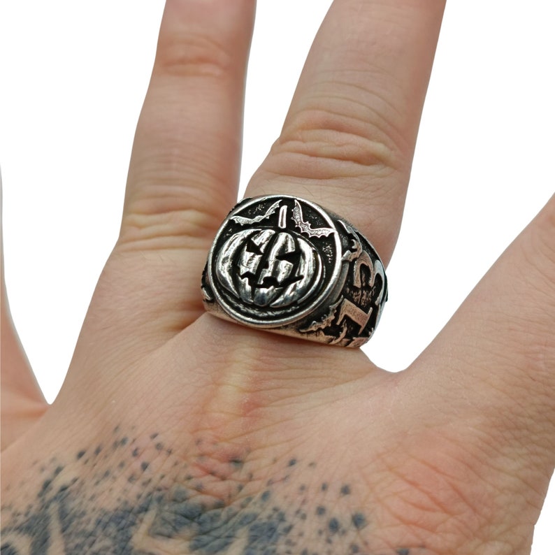 Puede incluir: Un anillo de plata con un dise&ntilde;o de calabaza detallado. El anillo se lleva en el dedo de una persona.