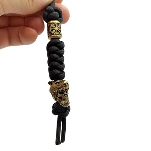 May include: Black paracord keychain with a brass skull bead and a brass bead with a symbol.