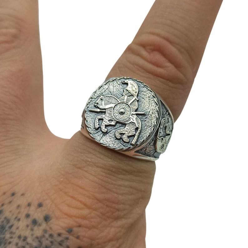 May include: A silver ring with a detailed design of a warrior on horseback. The ring is worn on a finger.