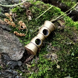 May include: A brass key chain with two holes in the middle. The key chain is on a bed of green moss.