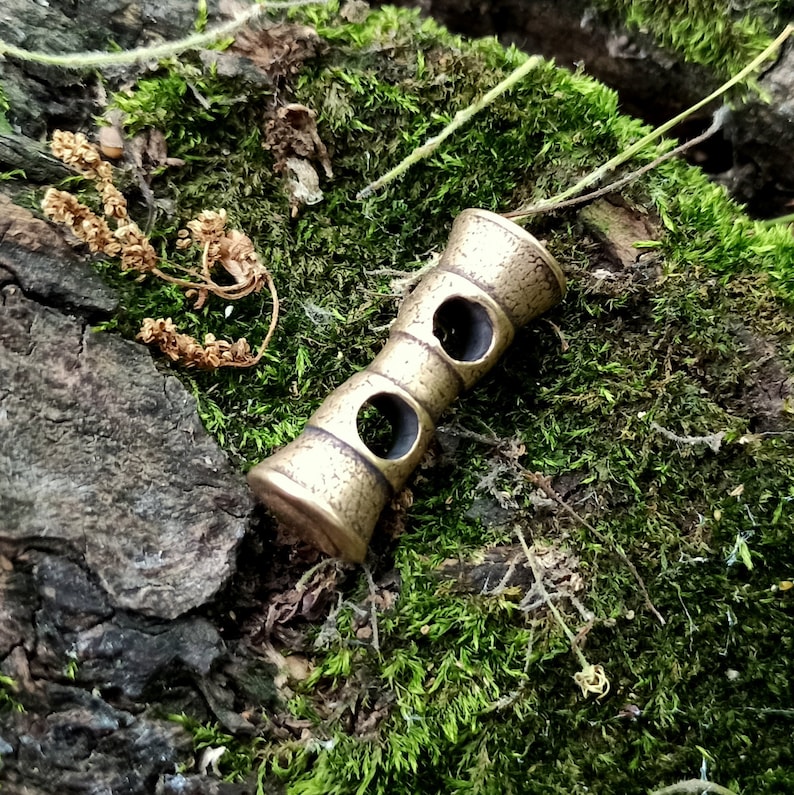 May include: A brass key chain with two holes in the middle. The key chain is on a bed of green moss.