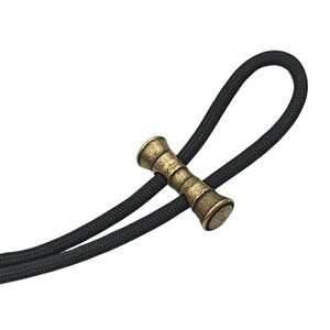 May include: A close-up of a brass toggle with a textured surface. The toggle is attached to a black cord.