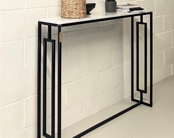 May include: A white marble top console table with a black metal frame. The table has a geometric design and features a rectangular top with a simple, clean design.