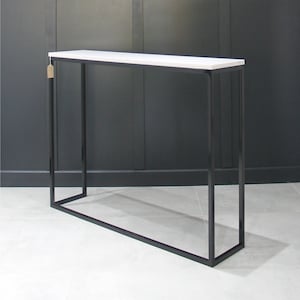May include: A white rectangular console table with a black metal frame. The table has a simple, modern design and is ideal for a hallway or entryway.