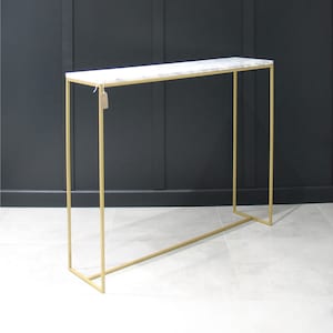 May include: A gold metal console table with a white marble top. The table has a simple, rectangular design and is perfect for a hallway or entryway.