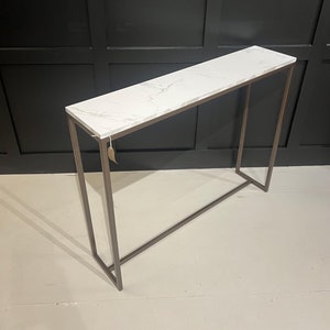 May include: A white marble top console table with a brown metal frame. The table has a simple, modern design and would be a great addition to any hallway or living room.