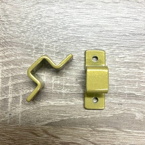 May include: Two gold metal brackets, one with a curved shape and the other with a rectangular shape. Both brackets have holes for mounting.