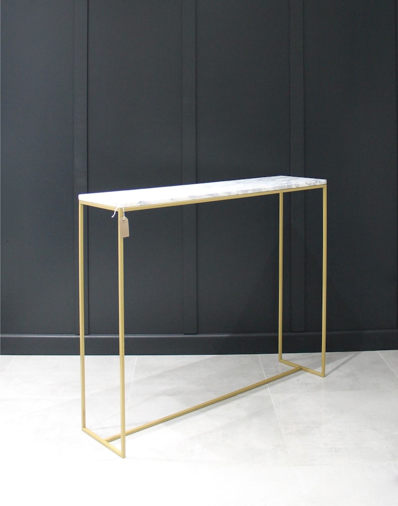 May include: A gold metal console table with a white marble top. The table has a simple, rectangular design and is perfect for a hallway or entryway.