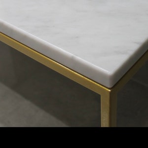May include: Close-up of a white marble table top with a gold metal frame. The marble has a subtle veining pattern.