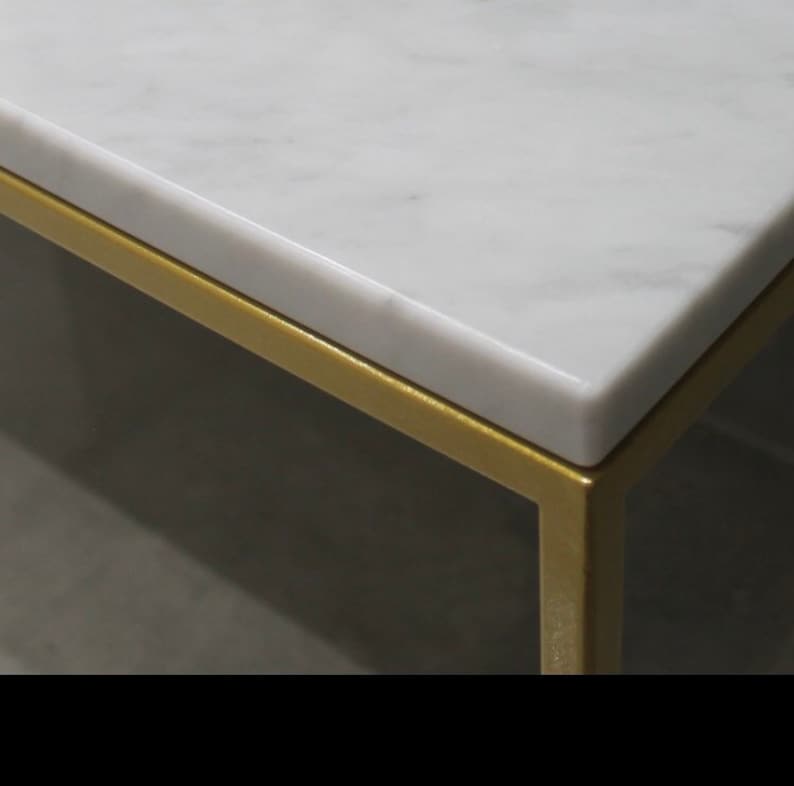 May include: Close-up of a white marble table top with a gold metal frame. The marble has a subtle veining pattern.