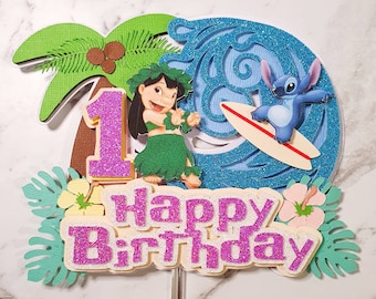 May include: A cake topper featuring Lilo and Stitch from Disney's Lilo & Stitch. Lilo is wearing a green hula skirt and a flower lei. Stitch is riding a surfboard on a blue wave. The topper also includes a palm tree, flowers, and the words "Happy Birthday" in pink glitter.