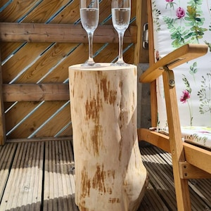 Puede incluir: Dos copas de champán llenas de agua con gas se encuentran sobre una mesa de tocón de madera rústica. La mesa está hecha de un tronco de árbol natural con una superficie rugosa y desgastada. La mesa está sobre una plataforma de madera.