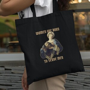 Può includere: Borsa tote nera con un dipinto di una donna che tiene la testa di un uomo. Il testo sulla borsa recita "Women are born to serve men."