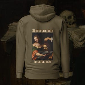 Könnte beinhalten: Ein khakifarbenes Kapuzenpullover mit einem Gemälde einer Frau, die einem Mann den Kopf wäscht. Der Text "Women are born to serve men" ist unter dem Gemälde gedruckt.