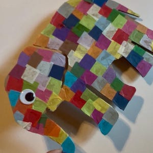 May include: A colorful, handmade paper elephant with a googly eye. The elephant is constructed from small, square pieces of tissue paper in various colors, including red, blue, green, and purple. The elephant's trunk is curled, and its ears are slightly raised.