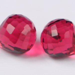May include: Two faceted, red gemstone beads. The beads are round with a pointed tip and have a high shine.