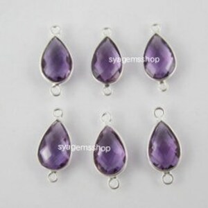 May include: Six amethyst teardrop gemstone beads with silver-toned jump rings. The beads are faceted and have a purple hue.