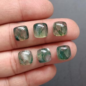 Pode incluir: Seis cabochões de ágata verde musgo com uma aparência translúcida e nublada. Os cabochões são de forma quadrada e têm um acabamento polido.