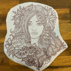 Pu&ograve; includere: Un designo intricato in marrone e bianco di un viso di donna con dettagli floreali. Il design &egrave; su uno sfondo bianco.