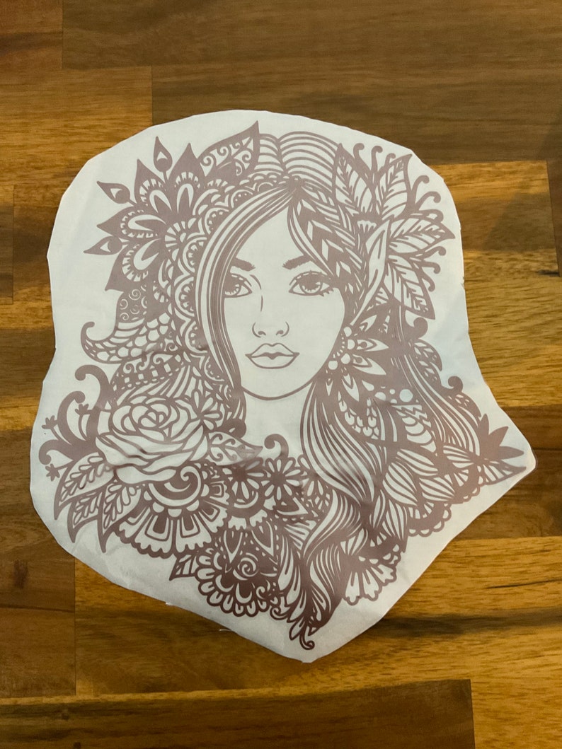 Pu&ograve; includere: Un designo intricato in marrone e bianco di un viso di donna con dettagli floreali. Il design &egrave; su uno sfondo bianco.