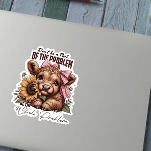 May include: A sticker depicting a cartoon calf with a pink bow and a sunflower. The calf is brown and white, and the sunflower is yellow. The sticker has the text: "Don't be a Part of the Problem, Be the Whole Problem."