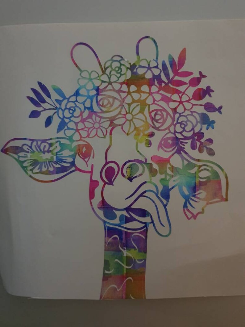 Pu&ograve; includere: Una giraffa colorata in stile acquerello con una corona di fiori. La giraffa ha un collo lungo e la lingua che sporge. I fiori sono in tonalit&agrave; di rosa, viola, blu e verde.