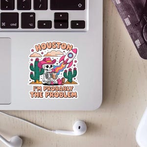 May include: A vibrant sticker design with a skeleton in a pink cowboy hat, holding a coffee cup, and set against cacti. A rocket ship and the text "HOUSTON I'M PROBABLY THE PROBLEM" are also included.