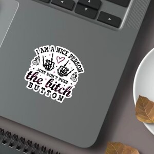 Peut inclure: Un autocollant blanc avec le texte "I AM A NICE PERSON JUST DON'T PUSH the bitch BUTTON". L'autocollant présente un motif de mains de squelette noir et blanc, des papillons et un cœur.