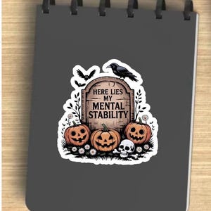 Könnte beinhalten: Ein Aufkleber mit einem Halloween-Design. Das Design umfasst drei geschnitzte Kürbisse, einen Grabstein mit dem Text "HERE LIES MY MENTAL STABILITY", einen Raben, Fledermäuse und einen Totenkopf. Der Aufkleber befindet sich auf grauem Hintergrund.