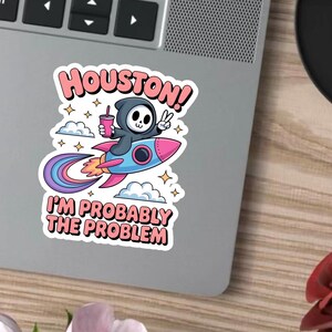 May include: A sticker with a cartoon grim reaper on a rocket. The rocket is blue and pink with a rainbow trail. The text on the sticker says "Houston! I'm Probably The Problem."