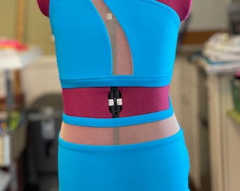 May include: A turquoise one-piece swimsuit with a mesh panel on the bodice and a high-cut leg. The swimsuit has a one-shoulder design.