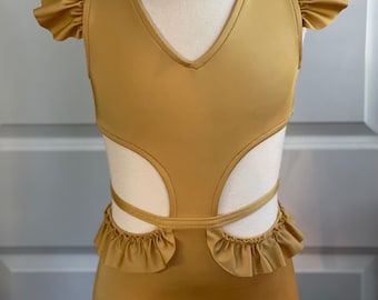 May include: A gold-colored leotard with a V-neckline and cut-out design. The leotard features ruffled cap sleeves and a ruffled waist detail. The garment is displayed on a mannequin.