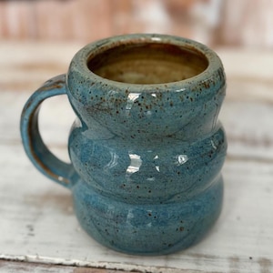 Puede incluir: Taza de cerámica hecha a mano con un diseño apilado único. La taza es de color azul verdoso moteado con interior y asa marrones. Ideal para café o té.