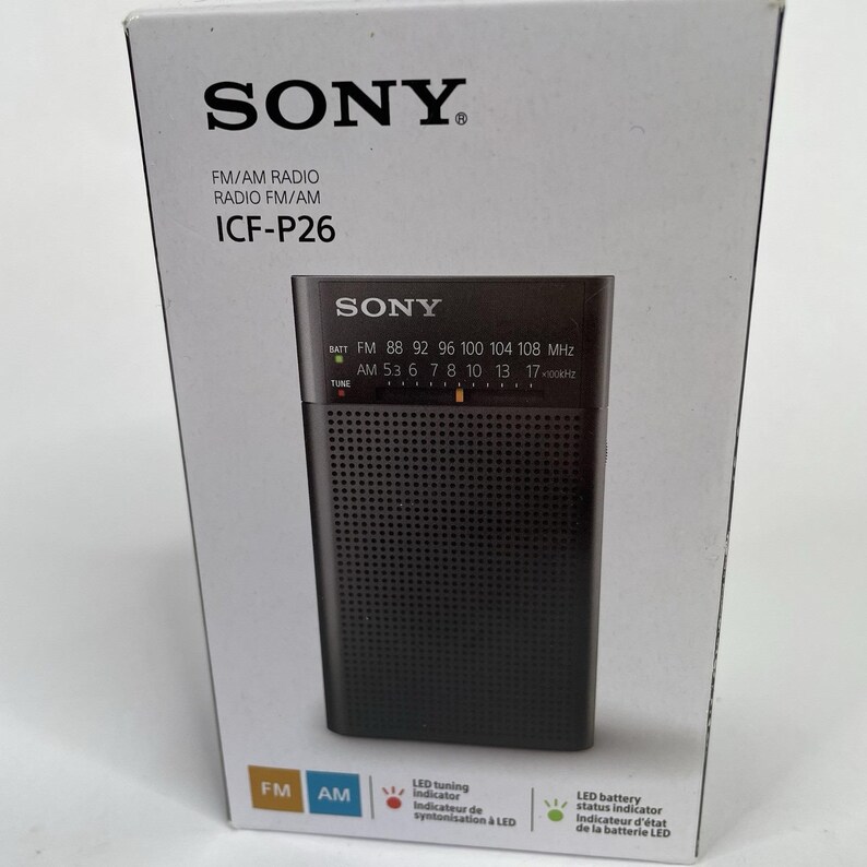 May include: A black Sony ICF-P26 FM/AM radio is shown in its packaging. The radio has a speaker grill and tuning dial. The box features the Sony logo and product information, including FM/AM radio specifications and LED indicators.