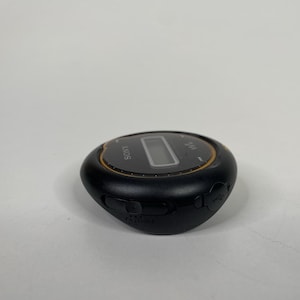 May include: Black Sony digital music player with a small LCD screen and gold trim. The device has several buttons and a USB port. The word "SONY" is printed on the top of the device.