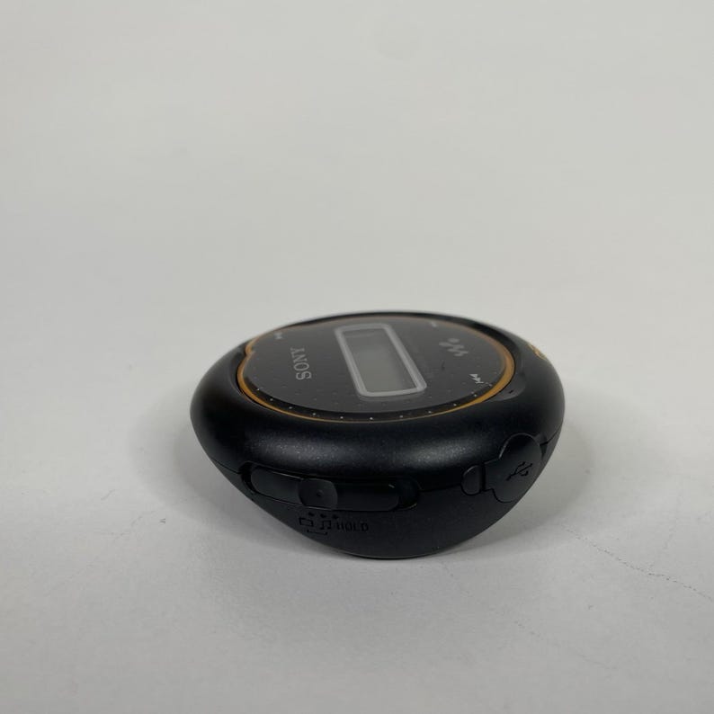 May include: Black Sony digital music player with a small LCD screen and gold trim. The device has several buttons and a USB port. The word "SONY" is printed on the top of the device.