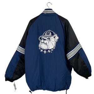 May include: A blue and black reversible jacket with a bulldog mascot logo on the back. The bulldog is wearing a hat with a "G" on it.
