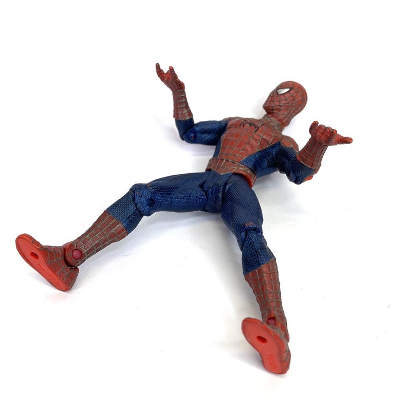 May include: A Spider-Man action figure in a dynamic pose, lying on its back with arms and legs spread. The figure is predominantly blue and red, with a detailed web pattern on the suit. The figure's red feet are visible.