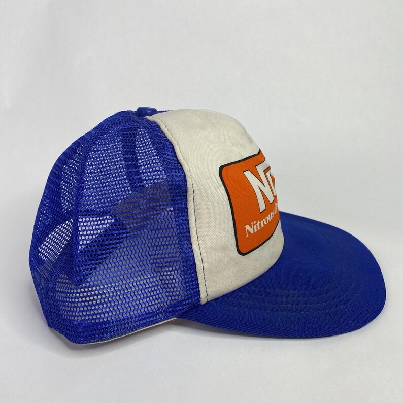 May include: A blue and white trucker hat with a curved brim. The hat features a mesh back and a front panel with the word "Nitrous" and the letter "N" in an orange rectangle.