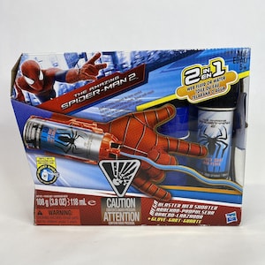 以下が含まれることがあります： アメイジング・スパイダーマン2のおもちゃセット。赤とオレンジ色のブラスターウェブシューター、青と赤の手袋、ウェブ液体のボトルが含まれています。パッケージにはスパイダーマンのグラフィックと「2 in 1 Web Fluid or Water」の文字が描かれています。