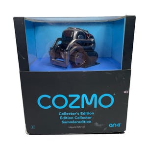 Peut inclure: Un robot Cozmo Édition Collector noir et argenté dans son emballage d'origine. La boîte est noire avec le mot "COZMO" en turquoise et le texte "Édition Collector" en blanc. Le robot est visible à travers une fenêtre en plastique transparent.