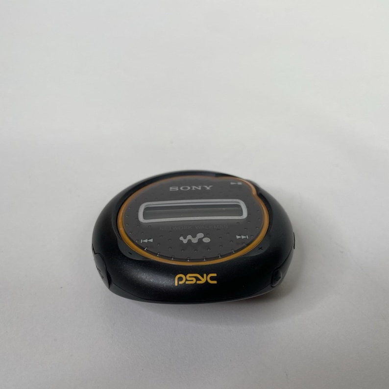 May include: A black and grey Sony digital music player with a circular design. The player has a small screen and control buttons. The word "SONY" is printed on the top, and "psyc" is printed on the bottom in yellow.