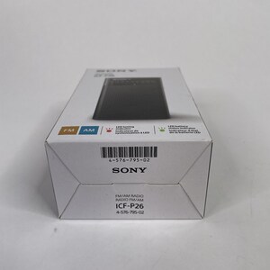 May include: A white box featuring a black radio, with the brand name "SONY" and model number "ICF-P26" printed on it. The box also displays "FM" and "AM" indicators, and other text in English and French.